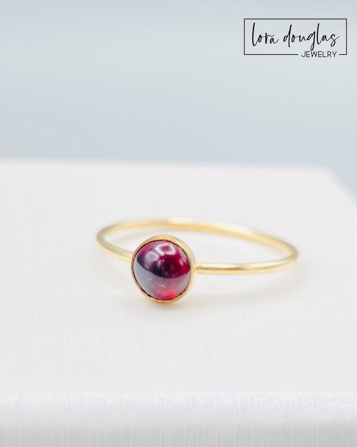 Detailed view of a 5mm garnet gemstone in a 14/20 gold filled solitaire setting, highlighting the contrast between the deep red stone and warm gold tones of this finished US size 6 birthstone ring.
