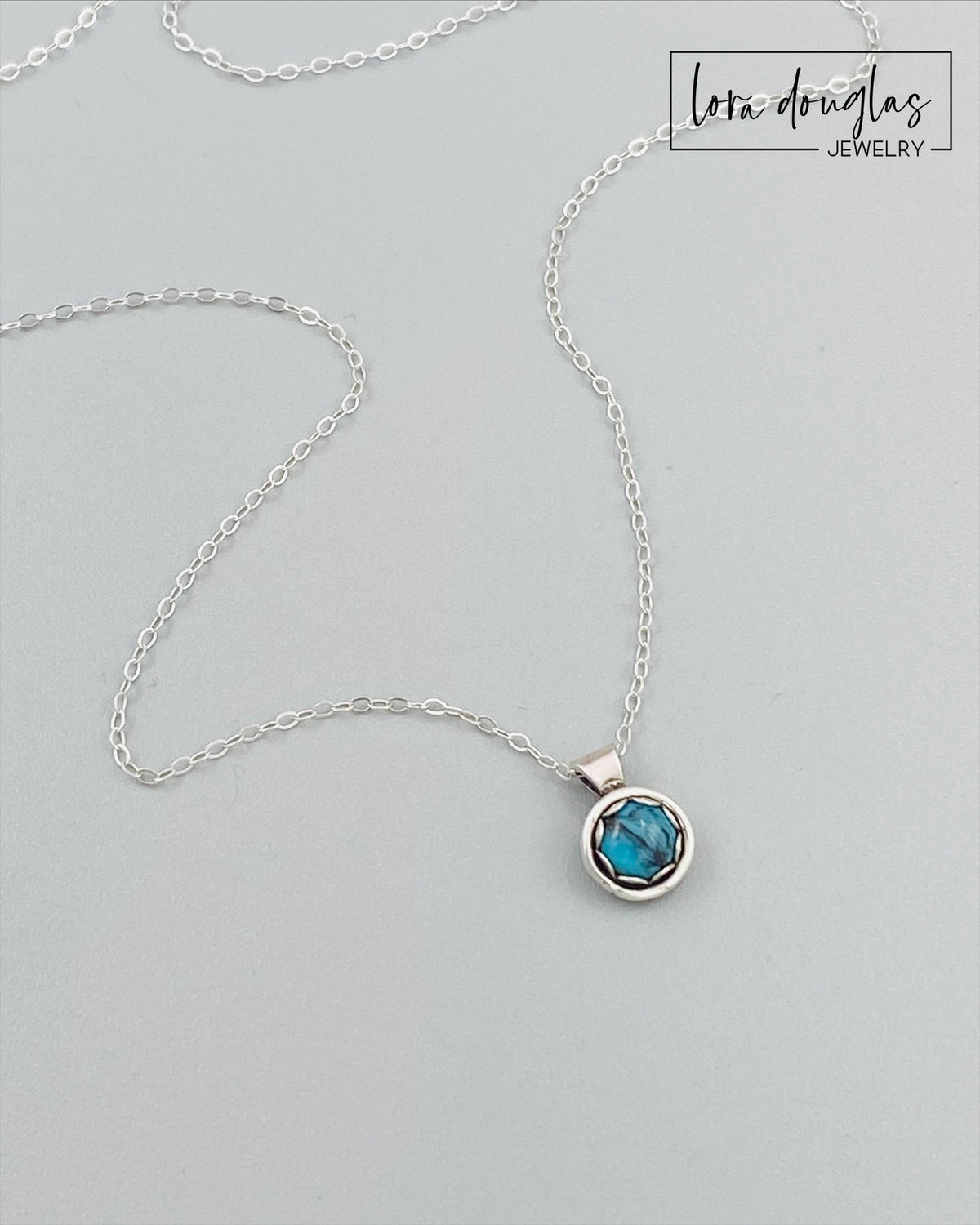 Detailed view of a 5mm natural turquoise gemstone in an 11mm x 8mm sterling silver pendant, highlighting the blue stone and silver setting of this petite necklace with an 18 inch antique patina chain.
