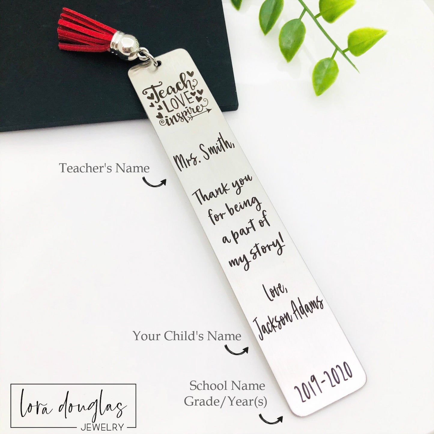 A stainless steel bookmarks with the phrases 'Teach Love Inspire' and 'Thank you for being a part of my story' engraved on them, presented in a navy blue velvet pouch with tassels.