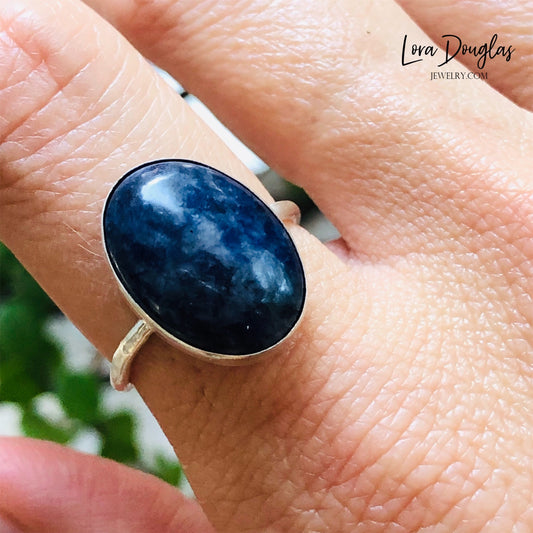 A sterling silver sodalite ring on a woman's finger, with a close-up on the ring showing the blue sodalite stone surrounded by a silver band.