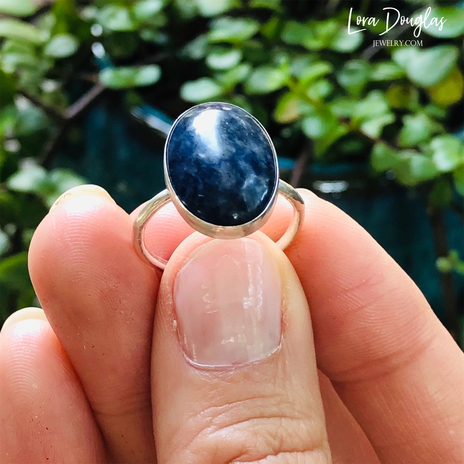 A sterling silver sodalite ring on a woman's finger, with a close-up on the ring showing the blue sodalite stone surrounded by a silver band.