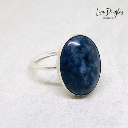 A sterling silver sodalite ring on a woman's finger, with a close-up on the ring showing the blue sodalite stone surrounded by a silver band.