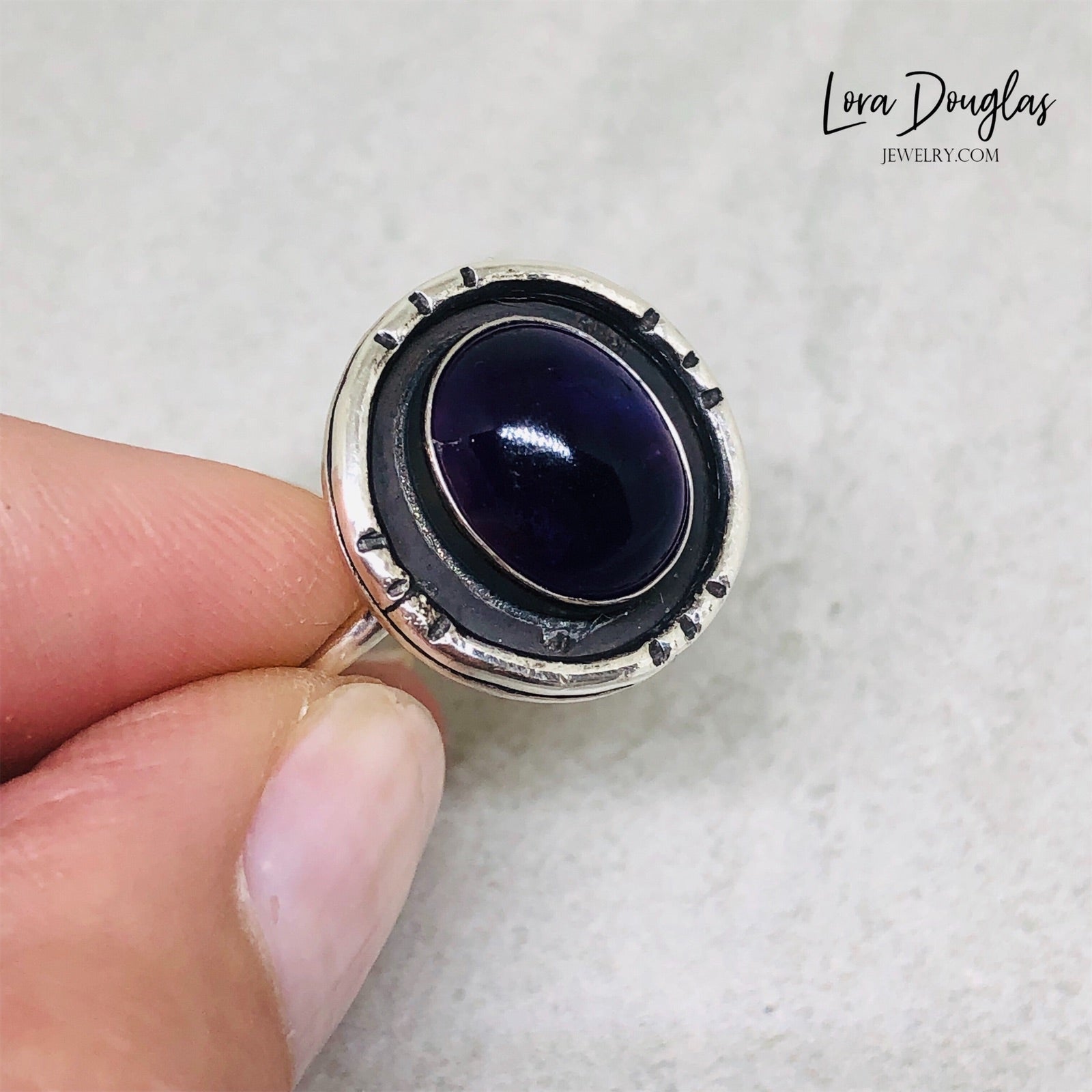 A sterling silver shadow box ring with a central amethyst stone, set in a circular silver setting.