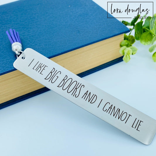 A stainless steel metal bookmark with an engraved message 'I like BIG BOOKS and I CANNOT LIE' hanging from a blue velvet drawstring pouch.