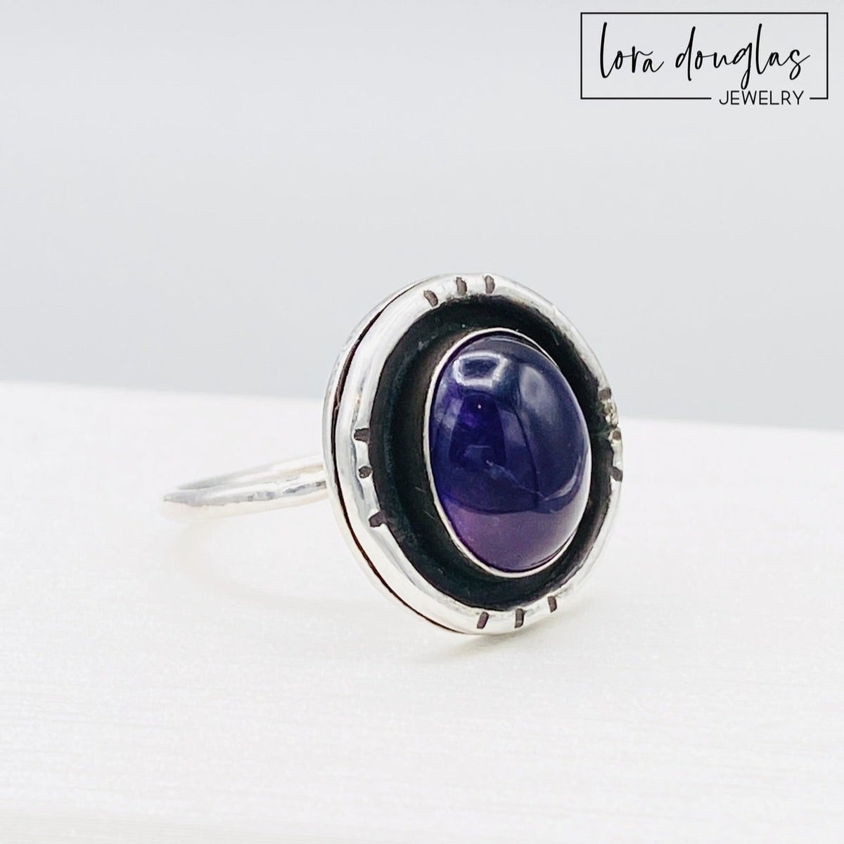 Handcrafted amethyst shadow box ring featuring a natural 12mm x 10mm purple gemstone in sterling and fine silver, shown as a finished US size 7.5 ring for lovers of artisan gemstone jewelry.
