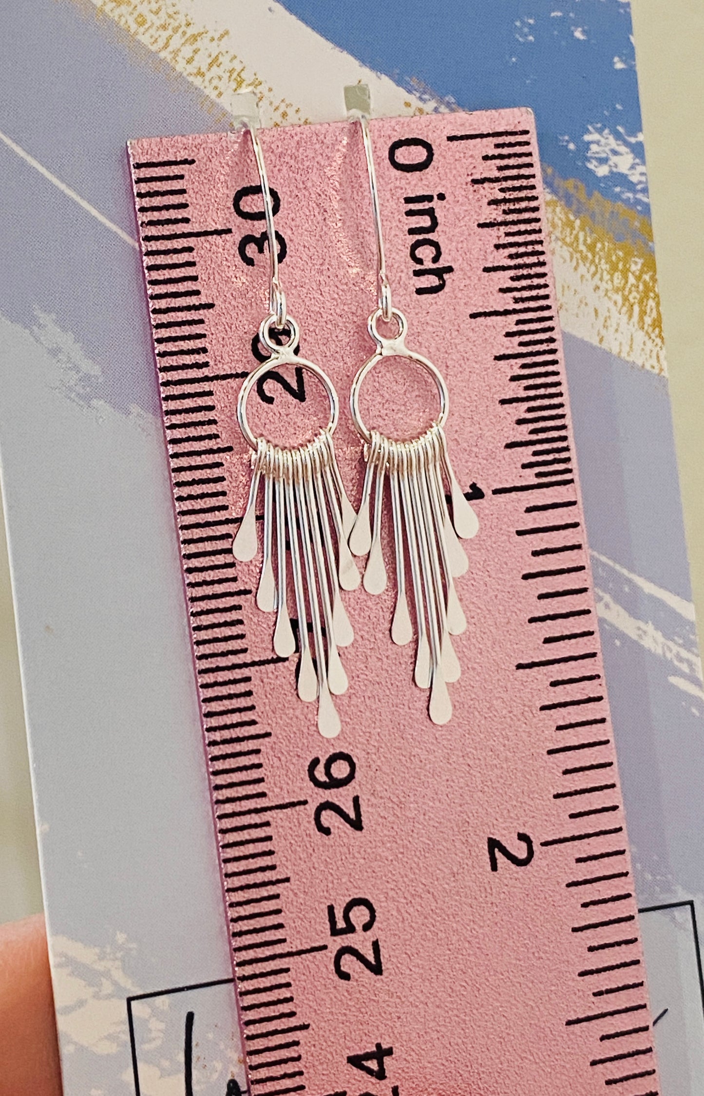 A pair of sterling silver fringe paddle earrings with a drop-style design, featuring small fringes dangling from a main hoop.