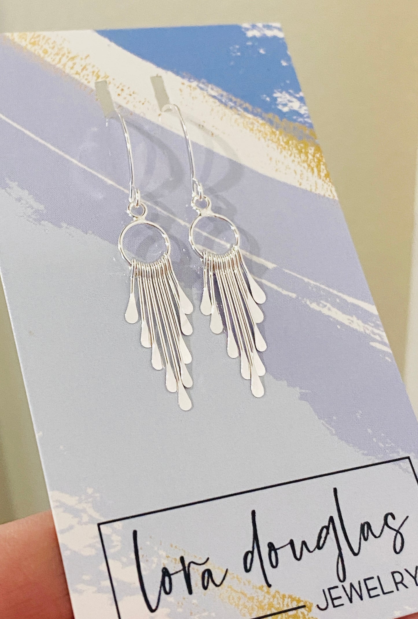 A pair of sterling silver fringe paddle earrings with a drop-style design, featuring small fringes dangling from a main hoop.