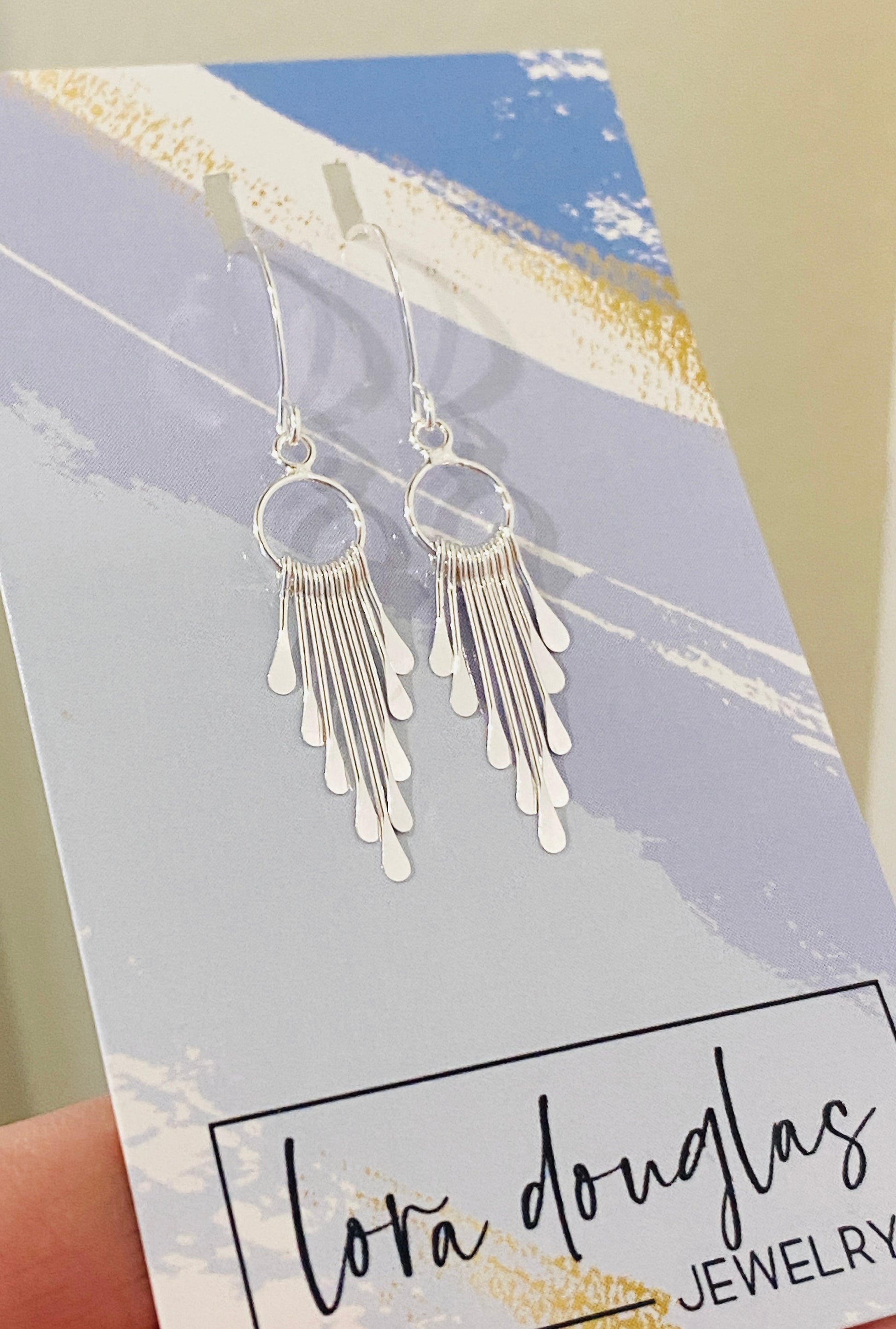 A pair of sterling silver fringe paddle earrings with a drop-style design, featuring small fringes dangling from a main hoop.