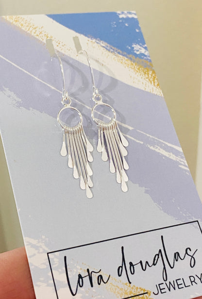 A pair of sterling silver fringe paddle earrings with a drop-style design, featuring small fringes dangling from a main hoop.