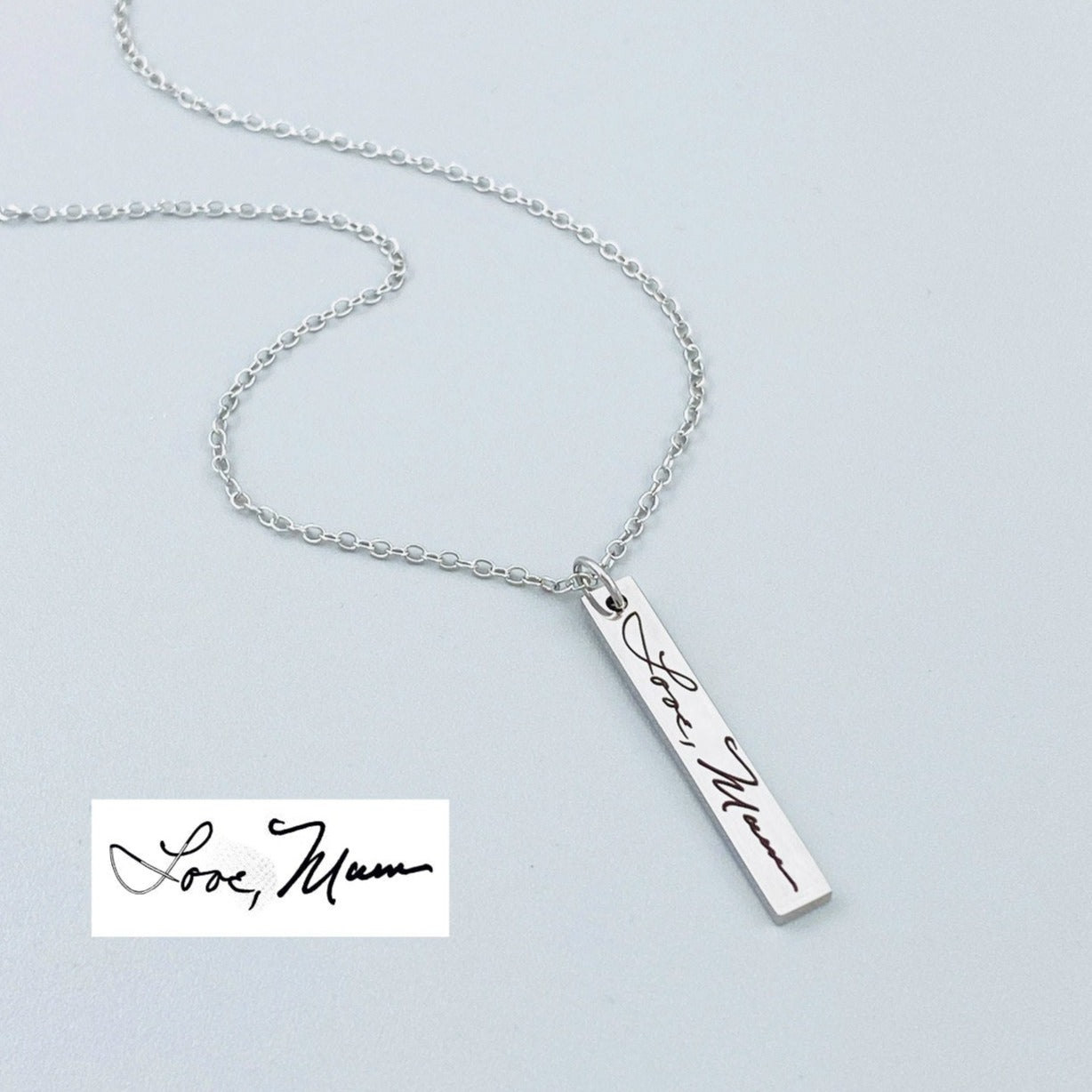 A silver stainless steel pendant necklace engraved with a handwritten message that reads 'Love Mom' on a chain.