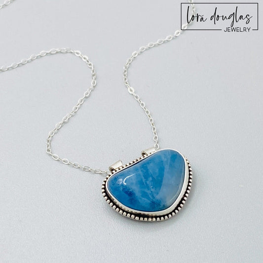 Natural aquamarine necklace featuring a blue gemstone in a 20mm x 23mm sterling silver pendant, paired with an 18 inch sterling silver chain with antique patina for distinctive gemstone jewelry.
