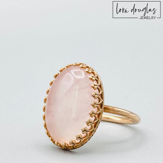Natural rose quartz ring featuring an 18mm x 13mm soft pink gemstone set in warm bronze, shown as a finished US size 7.5 statement ring for shoppers looking for meaningful natural stone jewelry.
