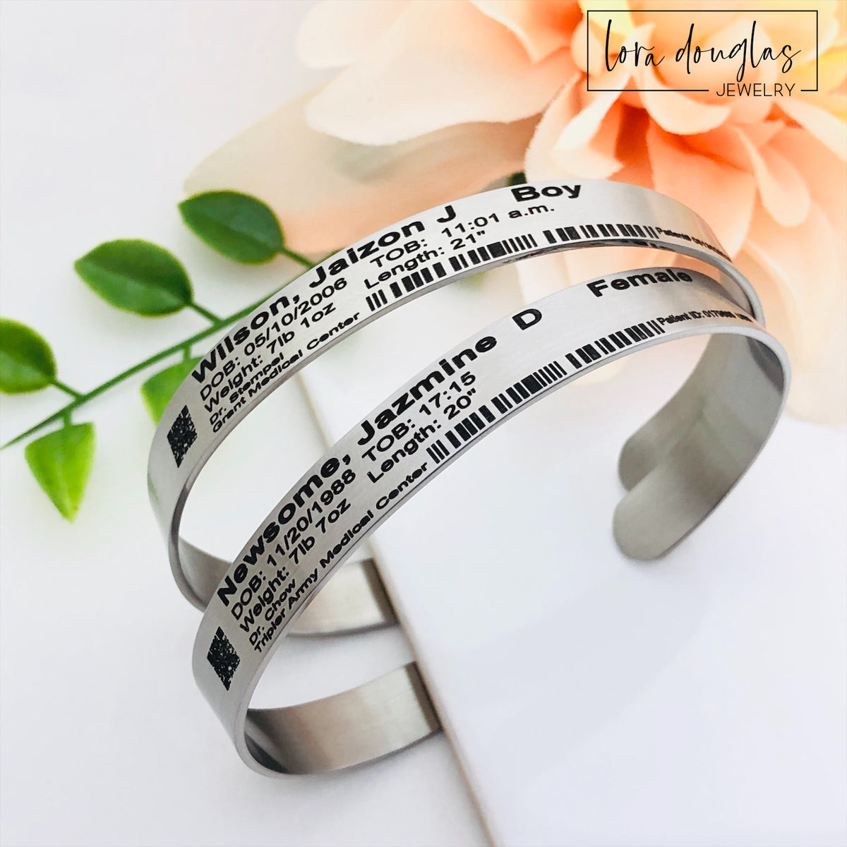 Personalized newborn ID bracelet with custom birth details, decorative barcode and QR code permanently laser engraved onto a stainless steel cuff, creating a unique baby keepsake for a memory box or new parent gift.
