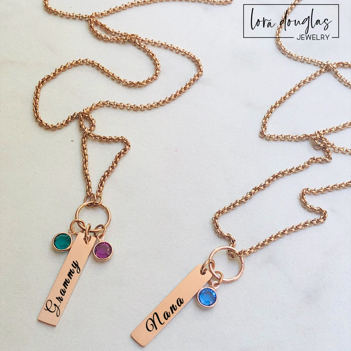 Rose gold necklaces with name charms and gemstones on a light background, featuring Lora Douglas Jewelry branding.