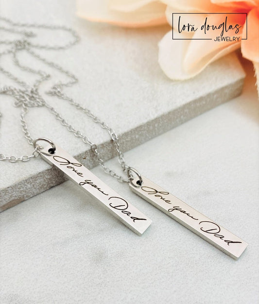 A silver stainless steel pendant necklace engraved with a handwritten message on a chain.