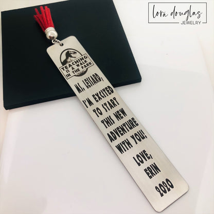 A stainless steel bookmark with an engraved message for a teacher, accompanied by a tassel and packaged for gift giving