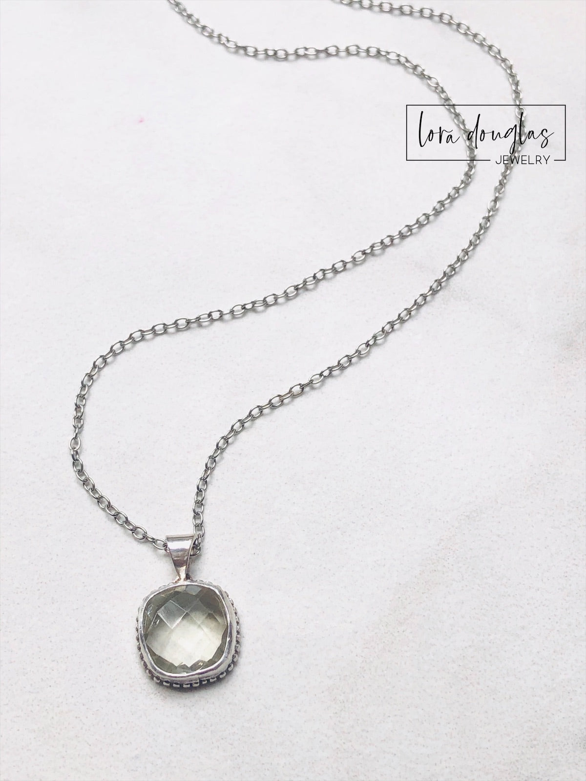 A sterling silver pendant necklace with a faceted green amethyst gemstone, attached to a silver chain.