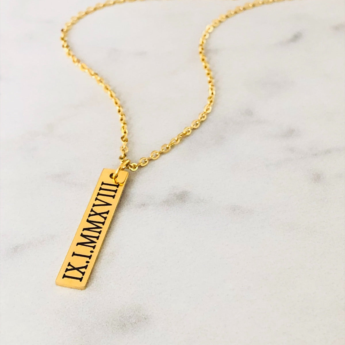 Gold necklace with Roman numeral pendant on a marble surface