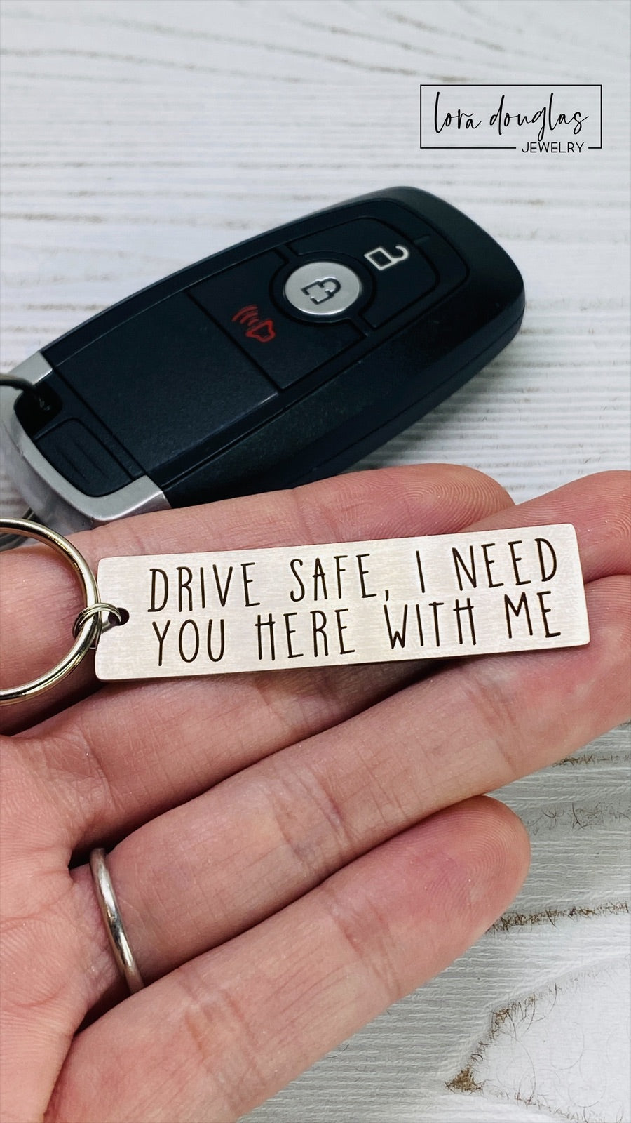 A metal key chain with the inscription 'DRIVE SAFE I NEED YOU HERE WITH ME' engraved on it.