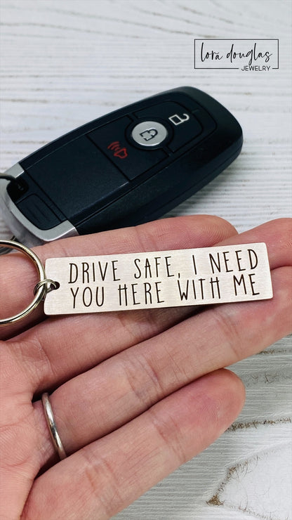 A metal key chain with the inscription 'DRIVE SAFE I NEED YOU HERE WITH ME' engraved on it.