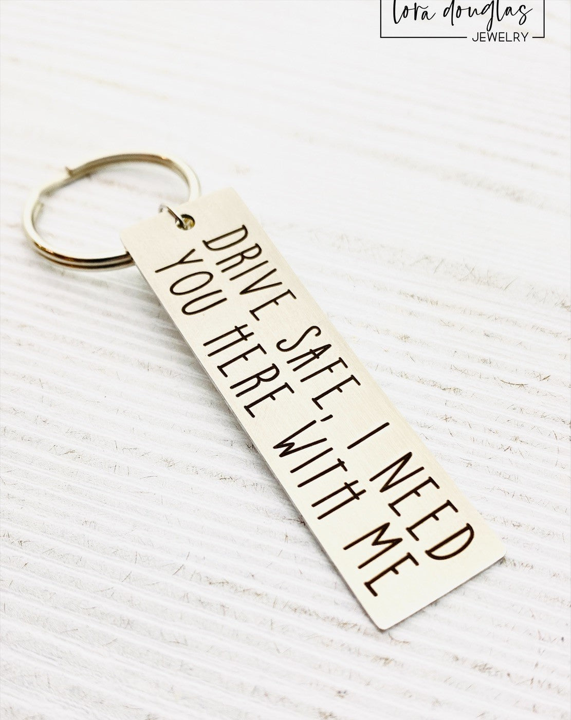 A metal key chain with the inscription 'DRIVE SAFE I NEED YOU HERE WITH ME' engraved on it.