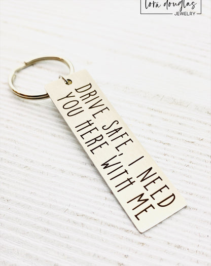 A metal key chain with the inscription 'DRIVE SAFE I NEED YOU HERE WITH ME' engraved on it.