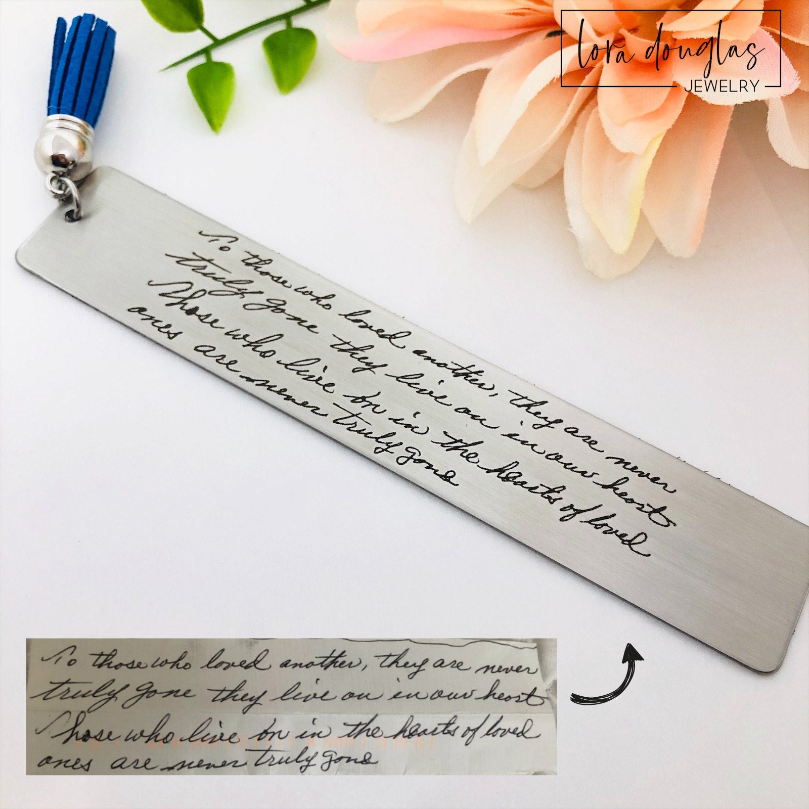 Two stainless steel bookmarks with engraved handwriting, with tassels, displayed on a wooden surface.