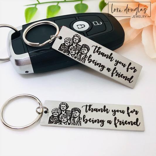 A stainless steel key chain with an engraved design of the Golden Girls characters and the text 'Thank you for being a friend'.
