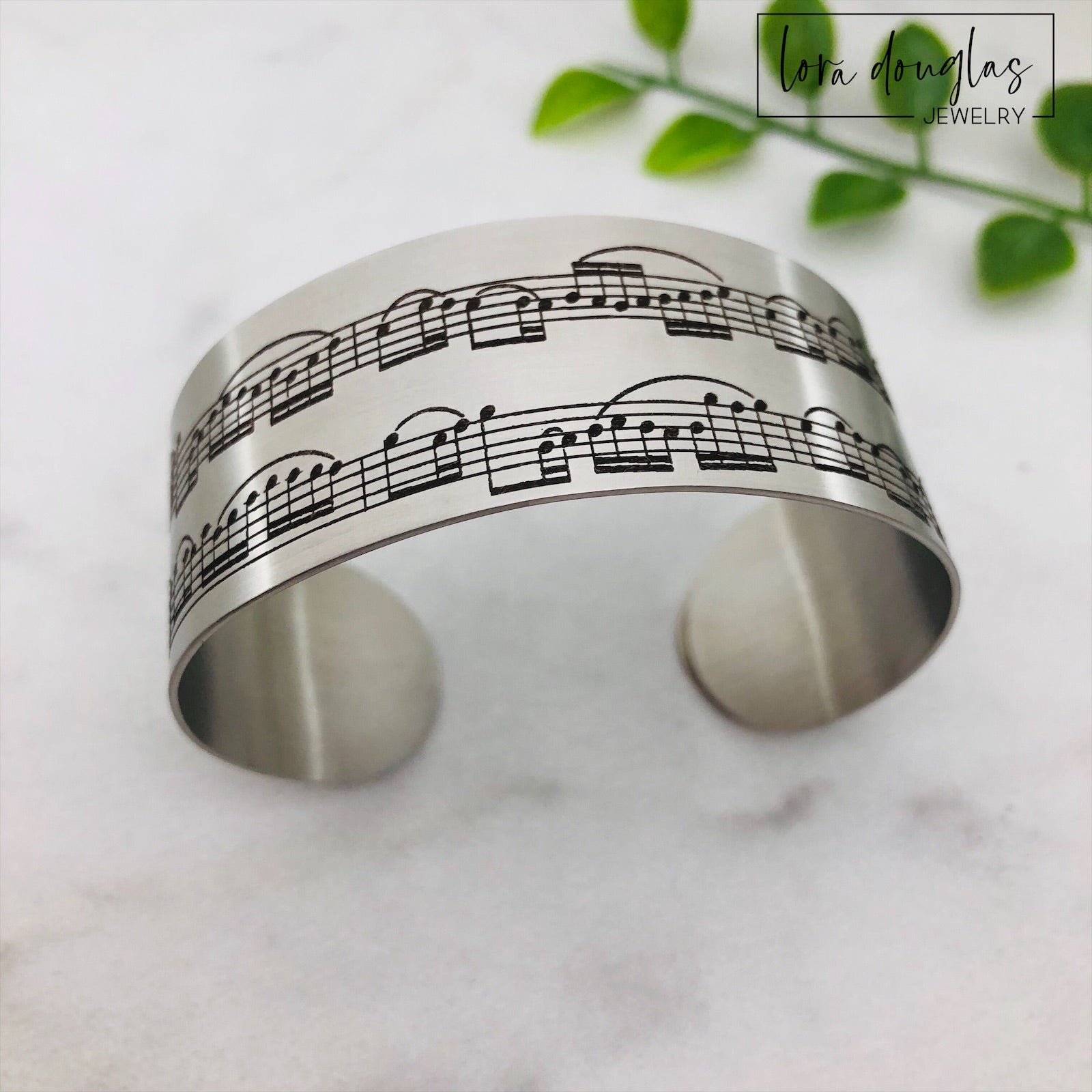 A stainless steel bracelet with sheet music engraving, displayed on a background of sheet music.