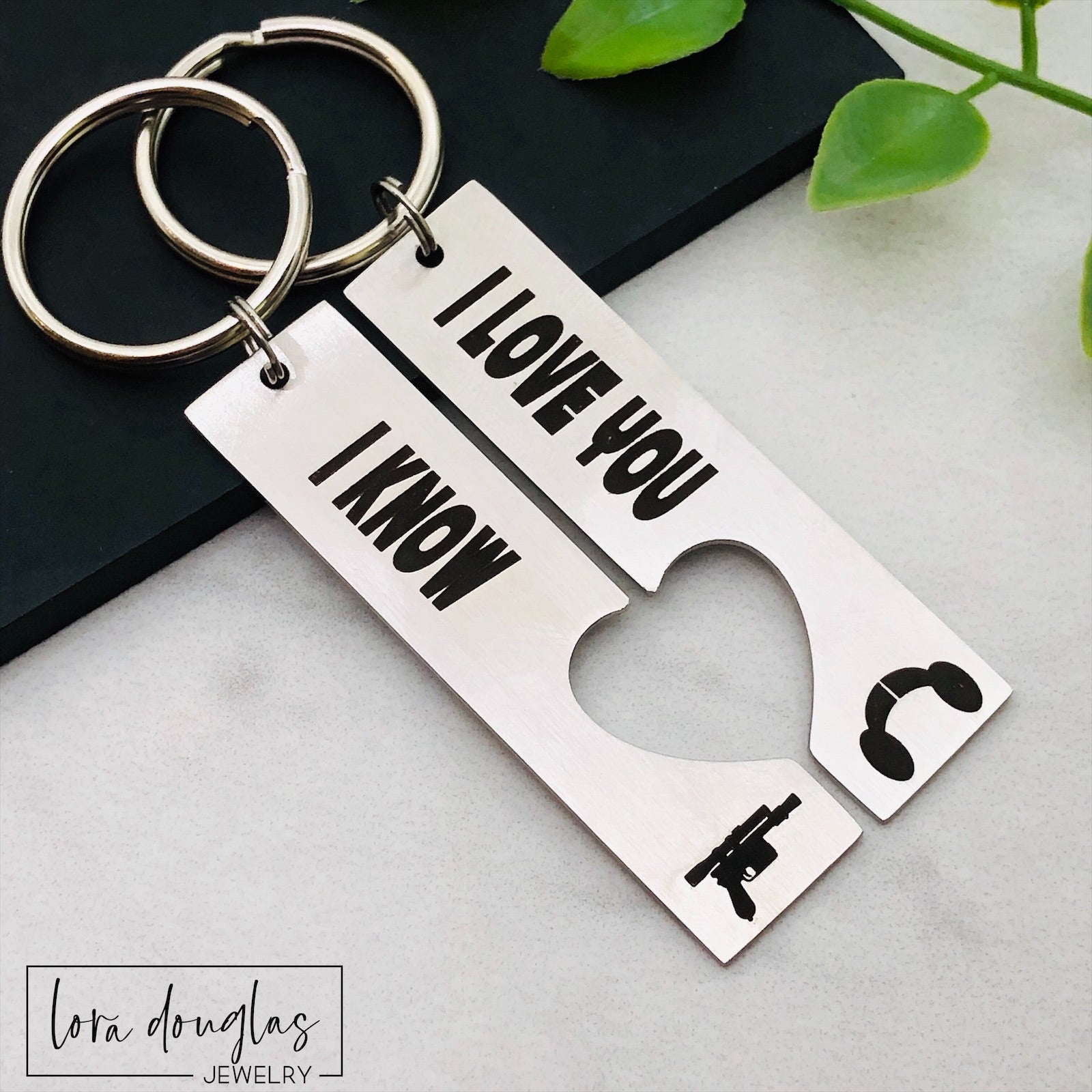 Two stainless steel key chains with the text 'I LOVE YOU, I KNOW' and a heart symbol engraved on them, placed on a flat surface.