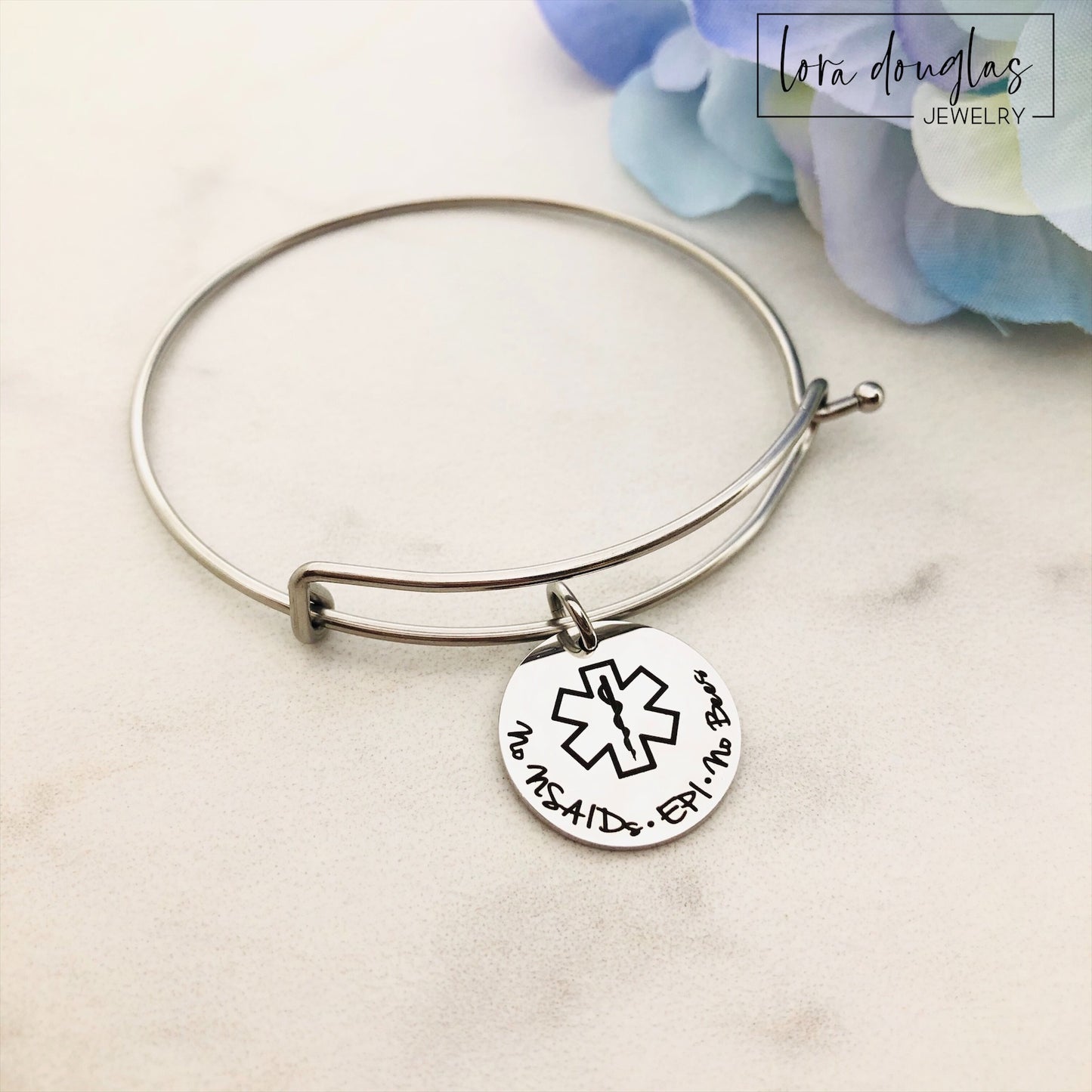 A stainless steel adjustable bangle bracelet with personalized medical alert charm.