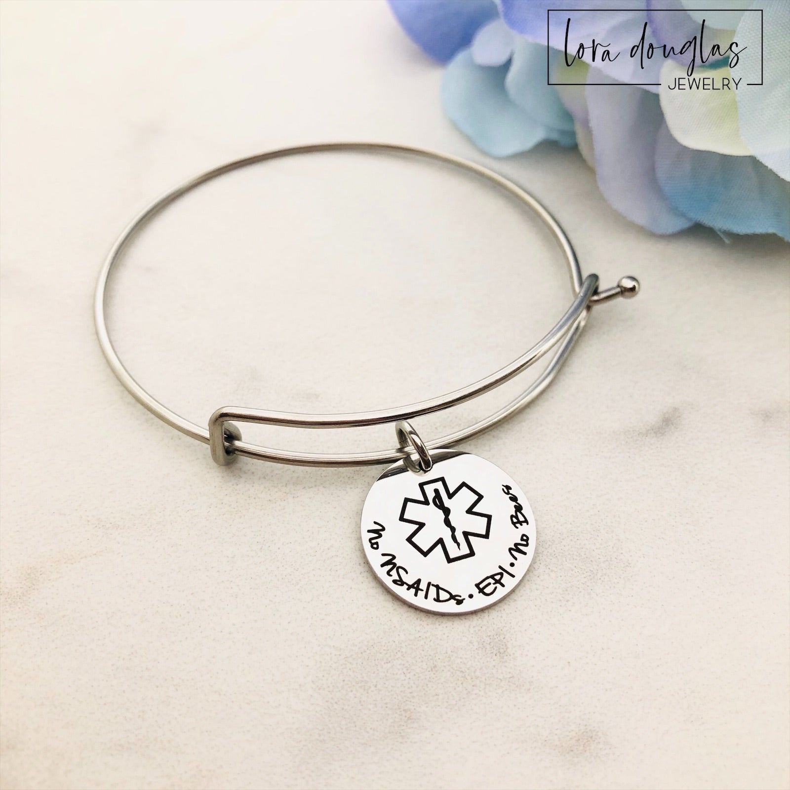 A stainless steel adjustable bangle bracelet with personalized medical alert charm.
