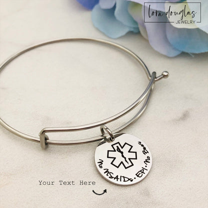 A stainless steel adjustable bangle bracelet with personalized medical alert charm.
