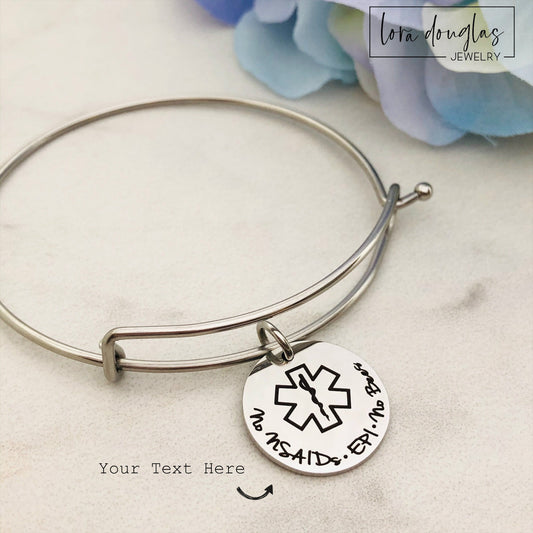 A stainless steel adjustable bangle bracelet with personalized medical alert charm.