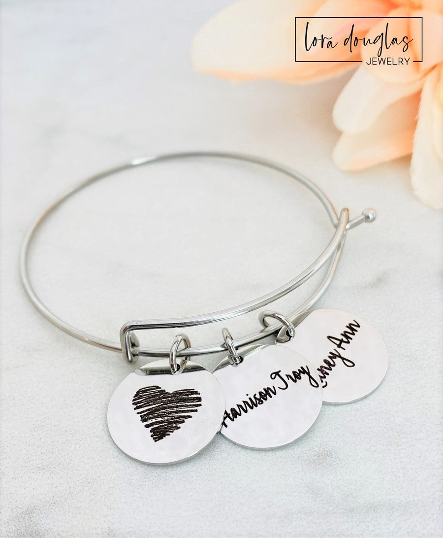 A collection of personalized jewelry items including necklaces, bracelets, and charms with engraved text and simple graphics on circular discs.