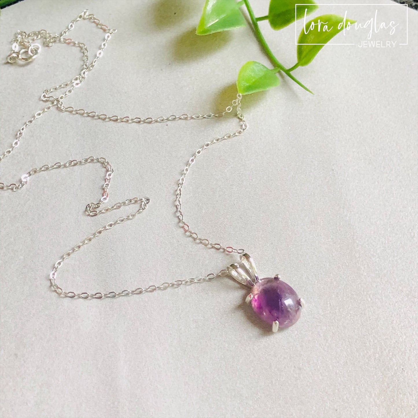 A sterling silver pendant necklace with a hand-cut amethyst gemstone, displayed on a silver chain against a black background.