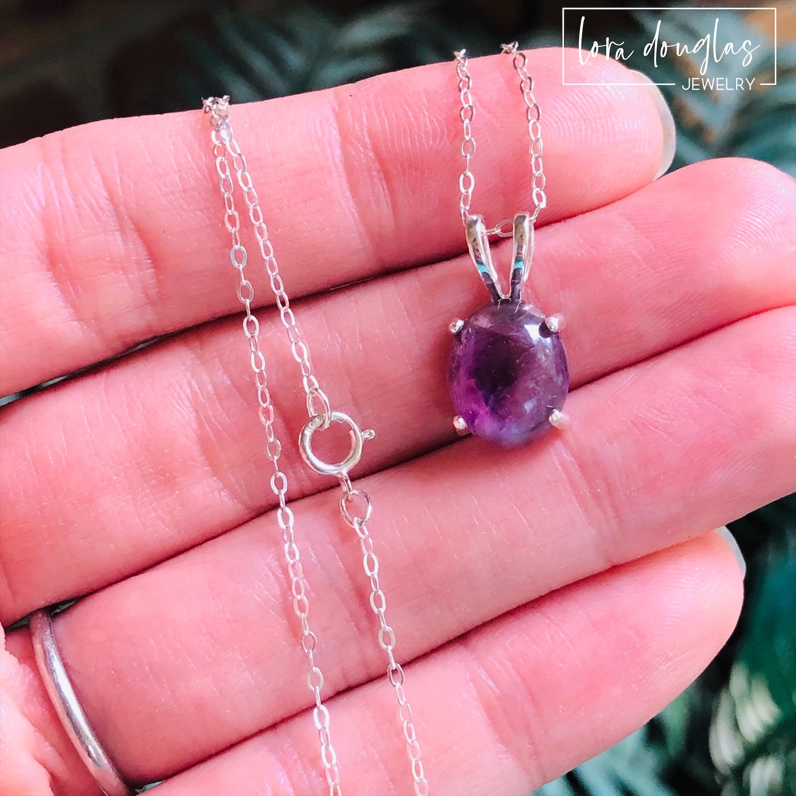 A sterling silver pendant necklace with a hand-cut amethyst gemstone, displayed on a silver chain against a black background.
