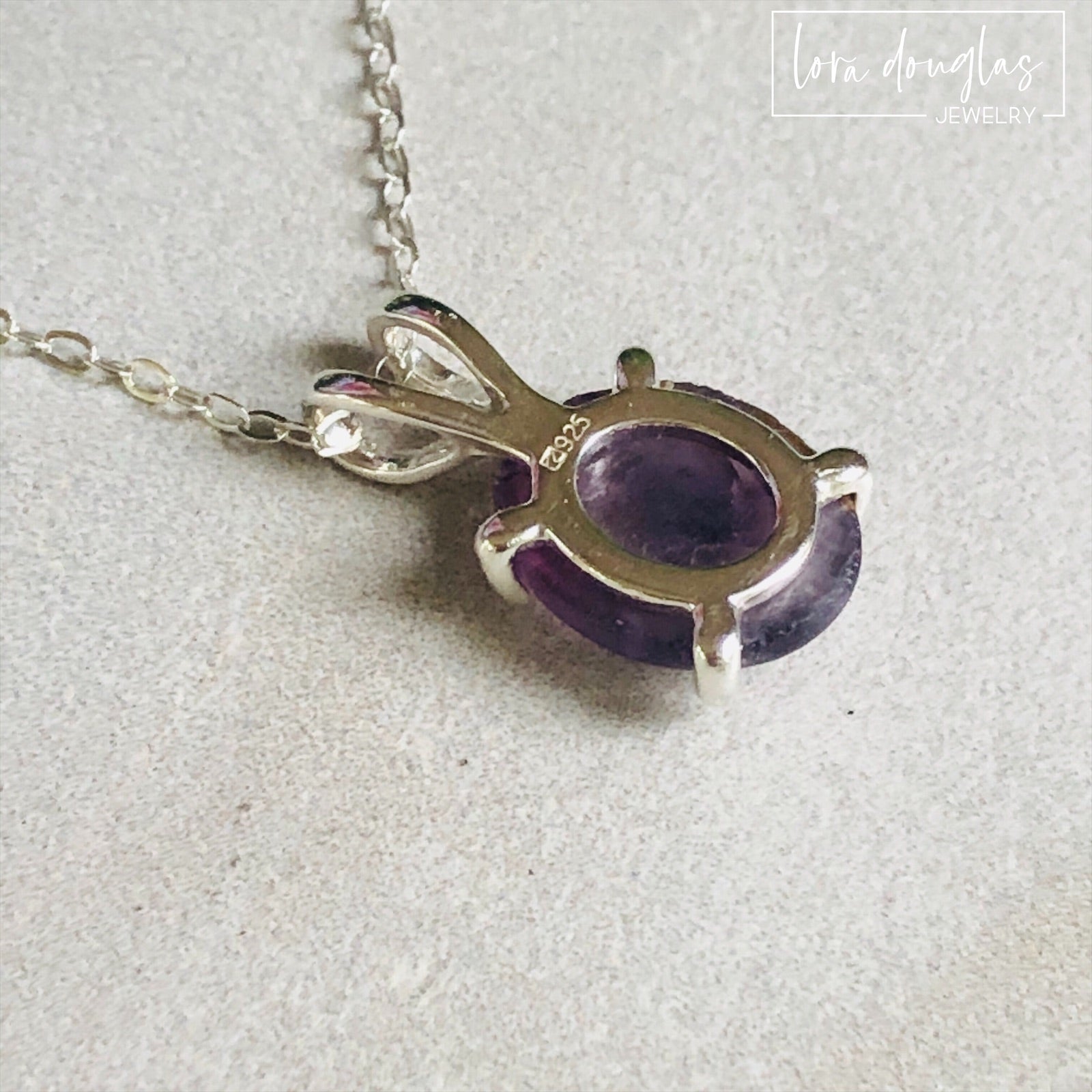 A sterling silver pendant necklace with a hand-cut amethyst gemstone, displayed on a silver chain against a black background.