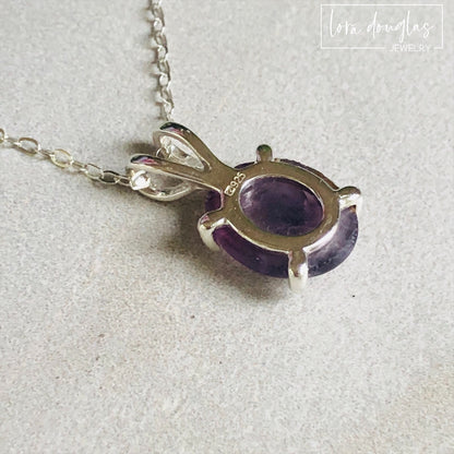 A sterling silver pendant necklace with a hand-cut amethyst gemstone, displayed on a silver chain against a black background.