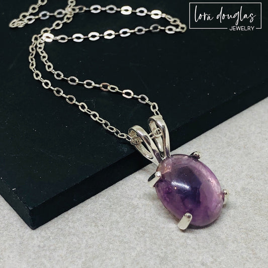 A sterling silver pendant necklace with a hand-cut amethyst gemstone, displayed on a silver chain against a black background.