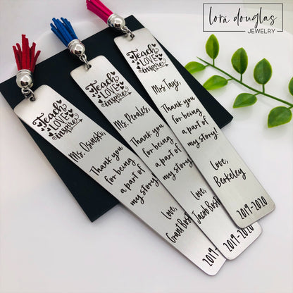 A set of stainless steel bookmarks with the phrases 'Teach Love Inspire' and 'Thank you for being my teacher' engraved on them, presented in a navy blue velvet pouch with tassels.