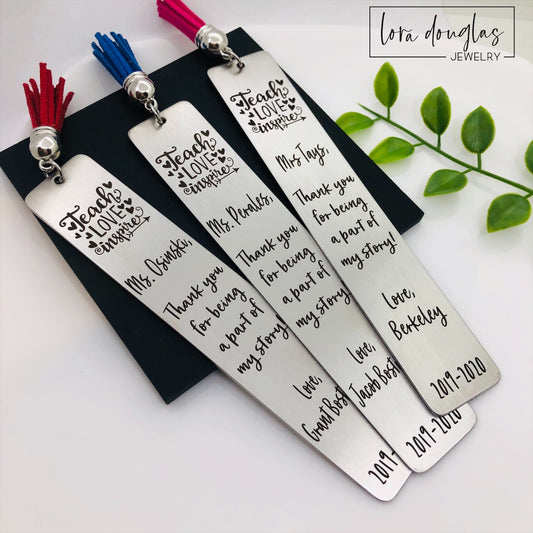 A set of stainless steel bookmarks with the phrases 'Teach Love Inspire' and 'Thank you for being my teacher' engraved on them, presented in a navy blue velvet pouch with tassels.