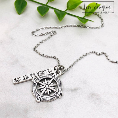 A silver compass necklace with a stainless steel pendant with personalized latitude and longitude coordinates