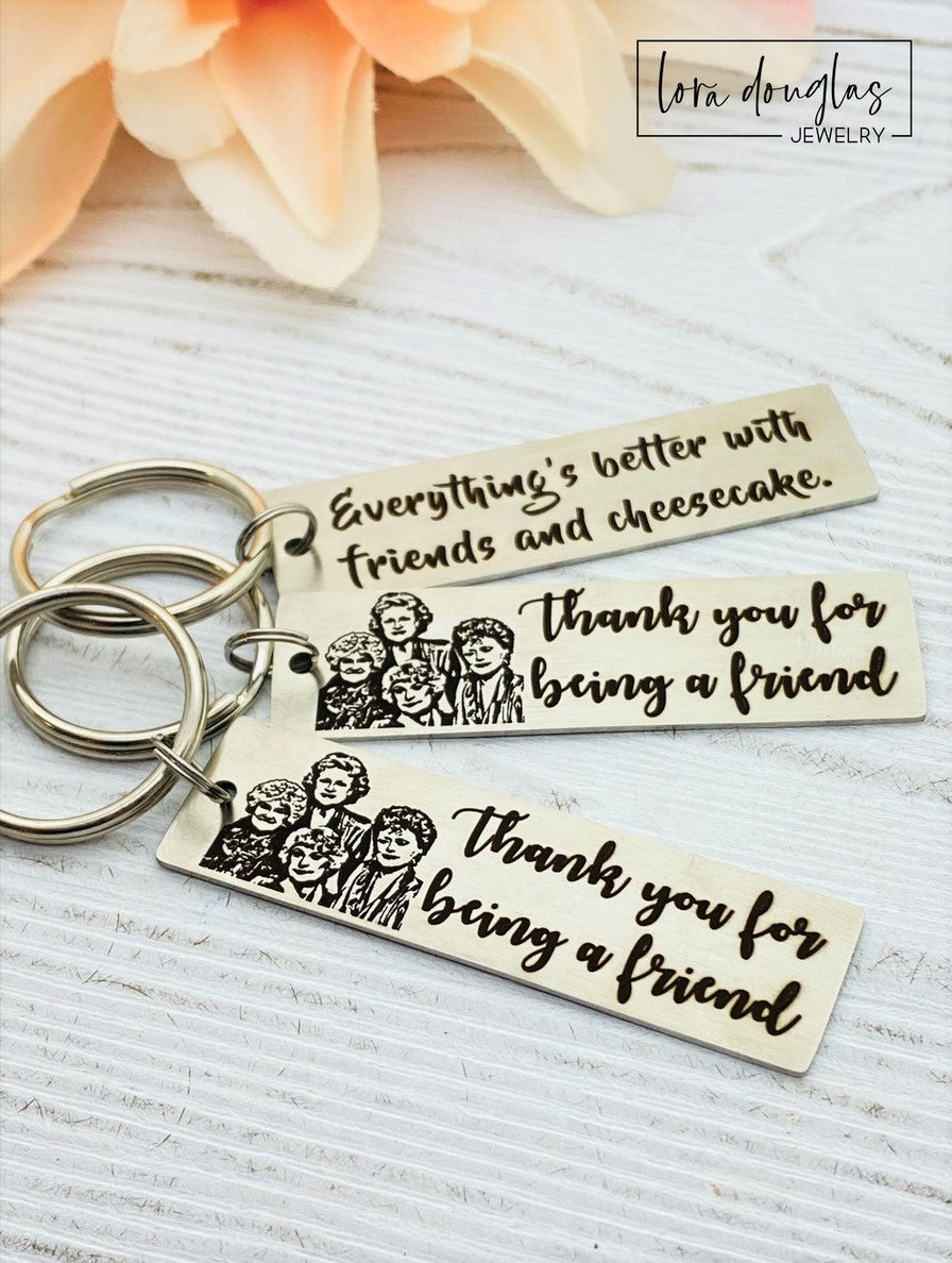 A stainless steel key chain with an engraved design of the Golden Girls characters and the text 'Thank you for being a friend'.