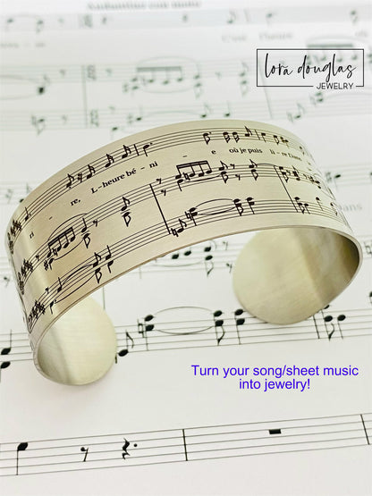 A stainless steel bracelet with sheet music engraving, displayed on a background of sheet music.