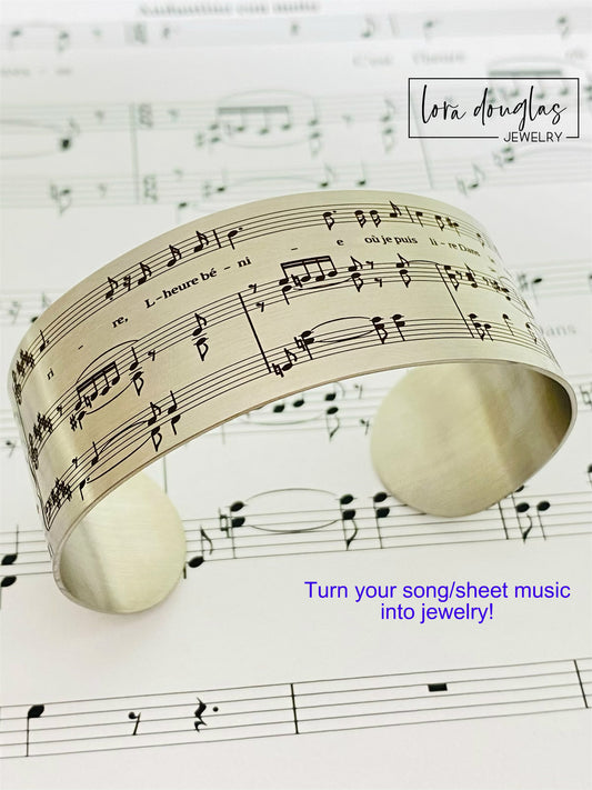 A stainless steel bracelet with sheet music engraving, displayed on a background of sheet music.