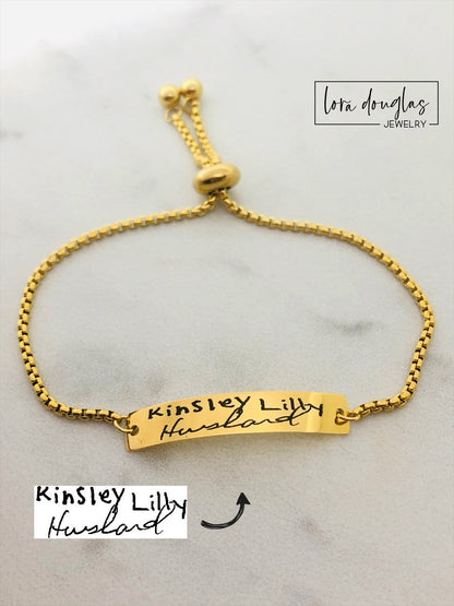 A gold bracelet with a bar pendant engraved with the handwritten message 