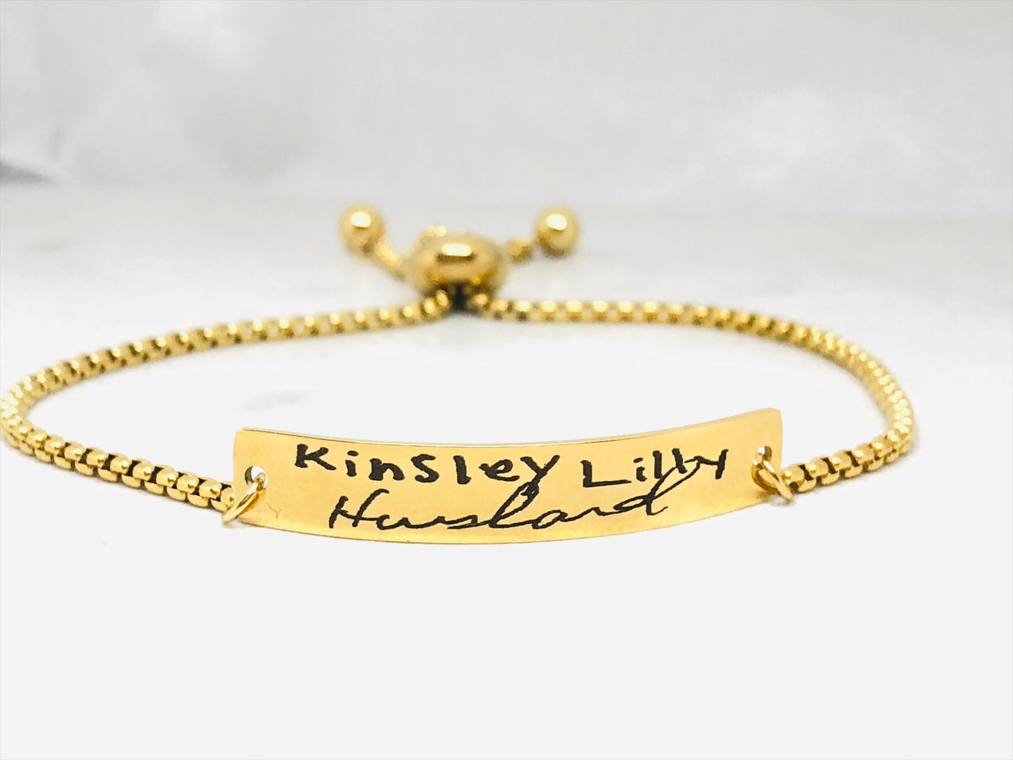 A gold bracelet with a bar pendant engraved with the handwritten message 