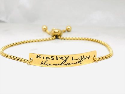 A gold bracelet with a bar pendant engraved with the handwritten message 