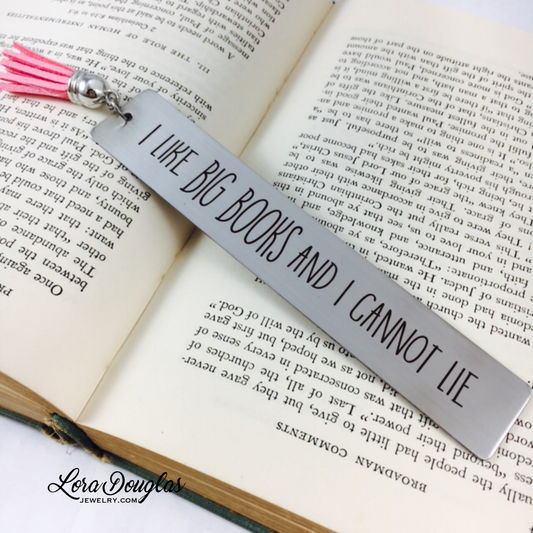 A stainless steel metal bookmark with an engraved message 'I like BIG BOOKS and I CANNOT LIE' hanging from a blue velvet drawstring pouch.